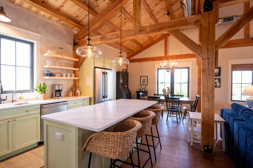Example of a mid-sized mountain style l-shaped light wood floor, brown floor and vaulted ceiling open concept kitchen design with a farmhouse sink, granite countertops, white backsplash, stainless steel appliances, an island and white countertops
