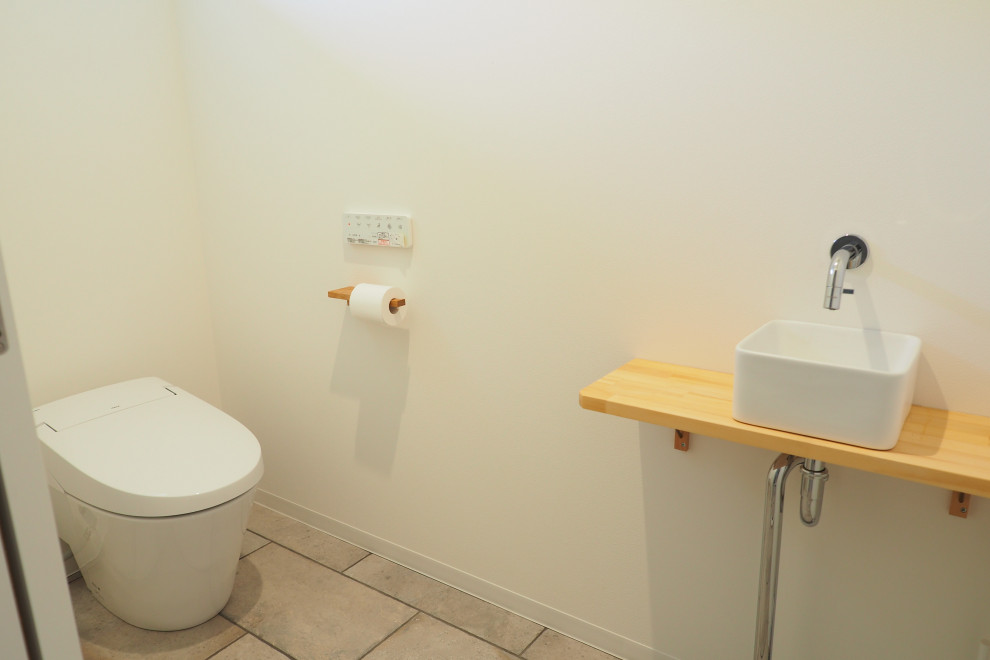 This is an example of a mid-sized beach style powder room in Other with dark wood cabinets, a one-piece toilet, gray tile, grey walls, vinyl floors, wood benchtops, beige floor, a freestanding vanity, wallpaper and wallpaper.