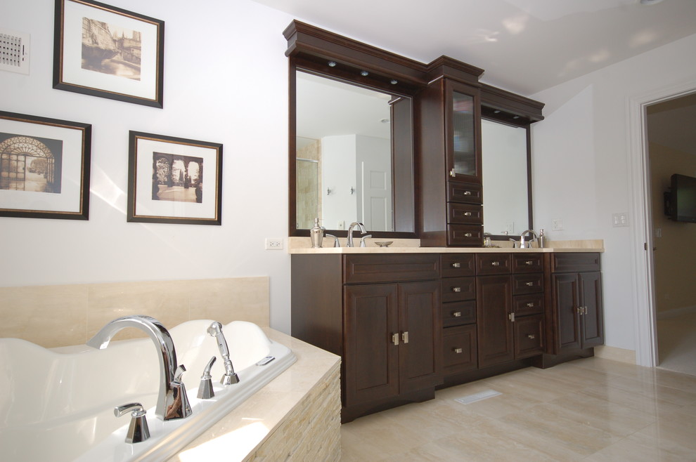 Expansive traditional master bathroom in Chicago with a corner tub, an undermount sink, dark wood cabinets, an open shower, a two-piece toilet, beige tile, grey walls, limestone floors and recessed-panel cabinets.