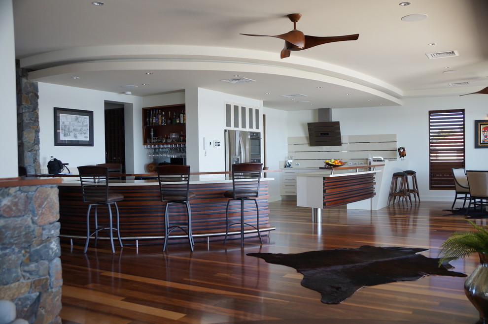 This is an example of a large tropical kitchen in Gold Coast - Tweed with solid surface benchtops, stainless steel appliances and medium hardwood floors.