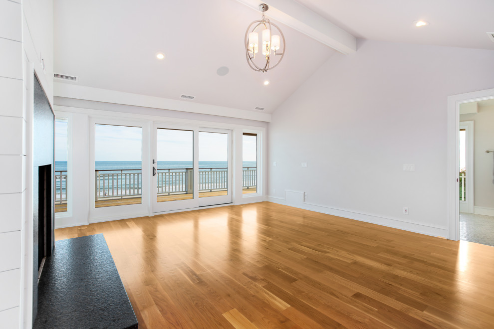 Cette photo montre une grande chambre parentale bord de mer avec un mur gris, parquet clair, une cheminée standard, un manteau de cheminée en pierre, un sol beige, un plafond voûté et du lambris de bois.