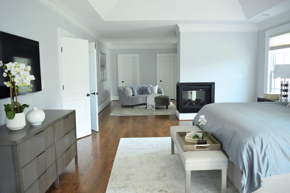 Inspiration for a large modern master bedroom in DC Metro with grey walls, medium hardwood floors, a two-sided fireplace, a plaster fireplace surround and brown floor.