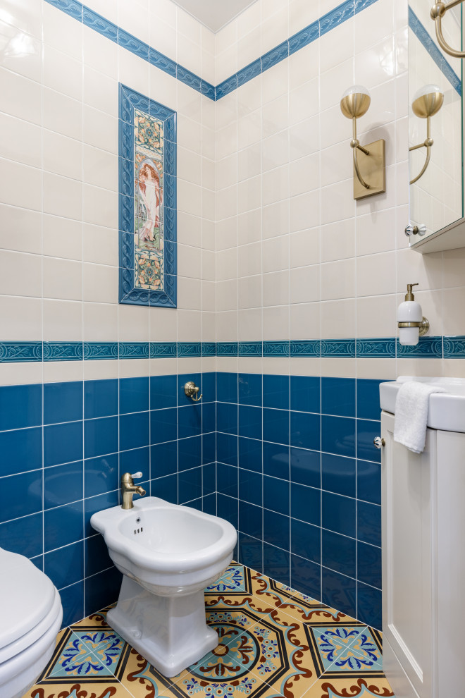 Aménagement d'un petit WC et toilettes classique avec un placard avec porte à panneau encastré, des portes de placard beiges, un bidet, un carrelage bleu, des carreaux de céramique, un mur beige, un sol en carrelage de porcelaine, un lavabo posé, un sol multicolore, un plan de toilette blanc et meuble-lavabo encastré.