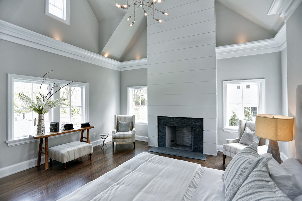This is an example of a mid-sized transitional master bedroom in New York with grey walls, dark hardwood floors, a standard fireplace, a wood fireplace surround and brown floor.