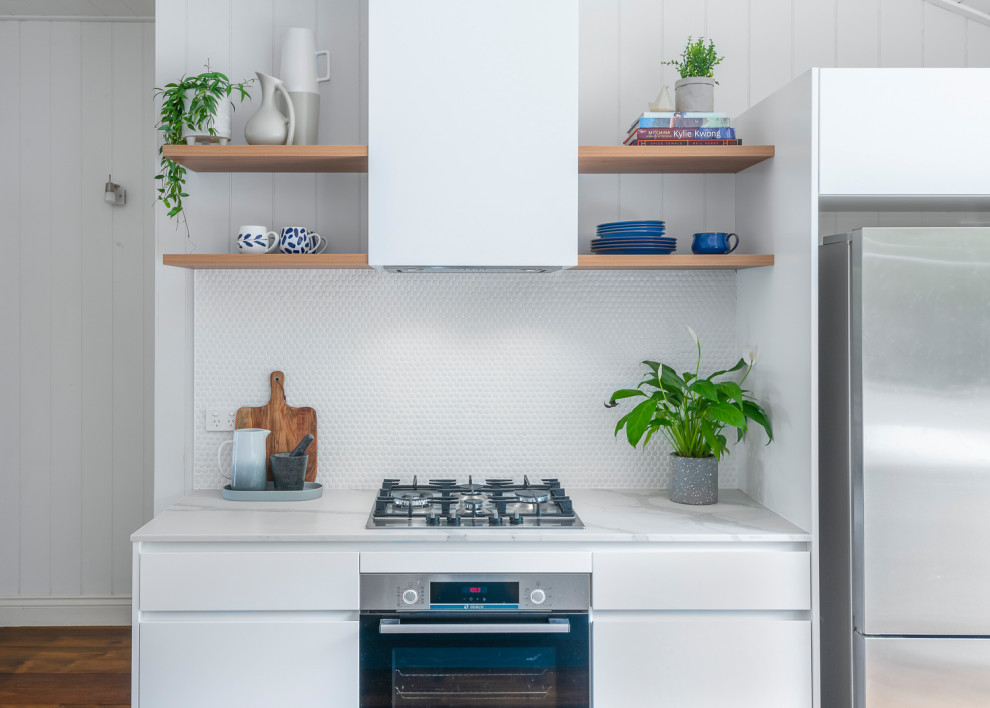 Design ideas for a mid-sized modern galley open plan kitchen in Brisbane with a double-bowl sink, blue cabinets, solid surface benchtops, white splashback, mosaic tile splashback, stainless steel appliances, dark hardwood floors, with island and white benchtop.