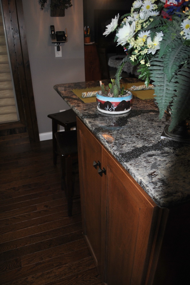Kitchen - brown floor kitchen idea with brown cabinets, beige backsplash, stainless steel appliances, an island and gray countertops