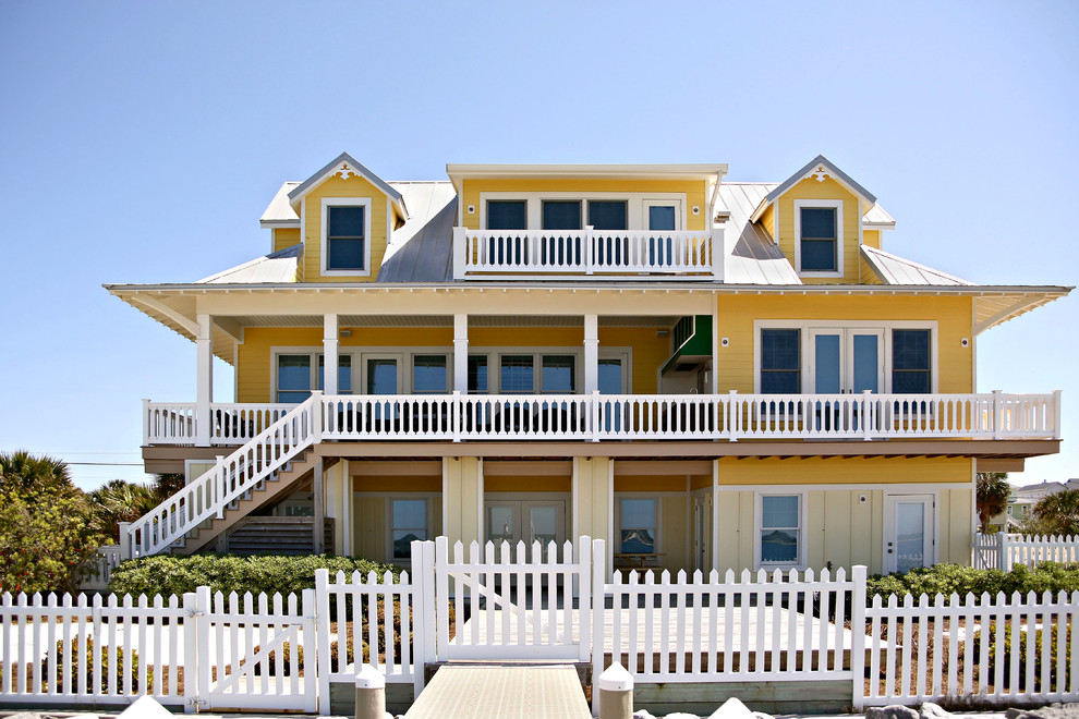 Photo of a small beach style three-storey yellow exterior in Miami with a gable roof.