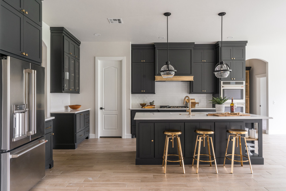 Large transitional l-shaped kitchen in Oklahoma City with an undermount sink, shaker cabinets, black cabinets, grey splashback, stainless steel appliances, with island, beige floor and grey benchtop.