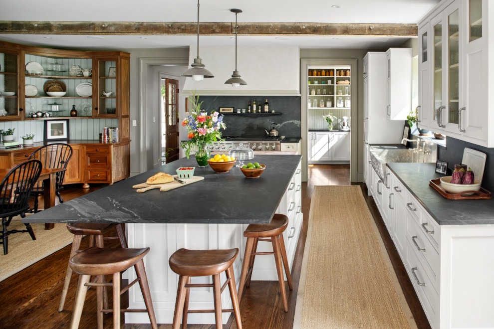 Photo of a traditional l-shaped eat-in kitchen in Philadelphia with a farmhouse sink, recessed-panel cabinets, white cabinets, stainless steel appliances, dark hardwood floors, with island, brown floor and grey benchtop.