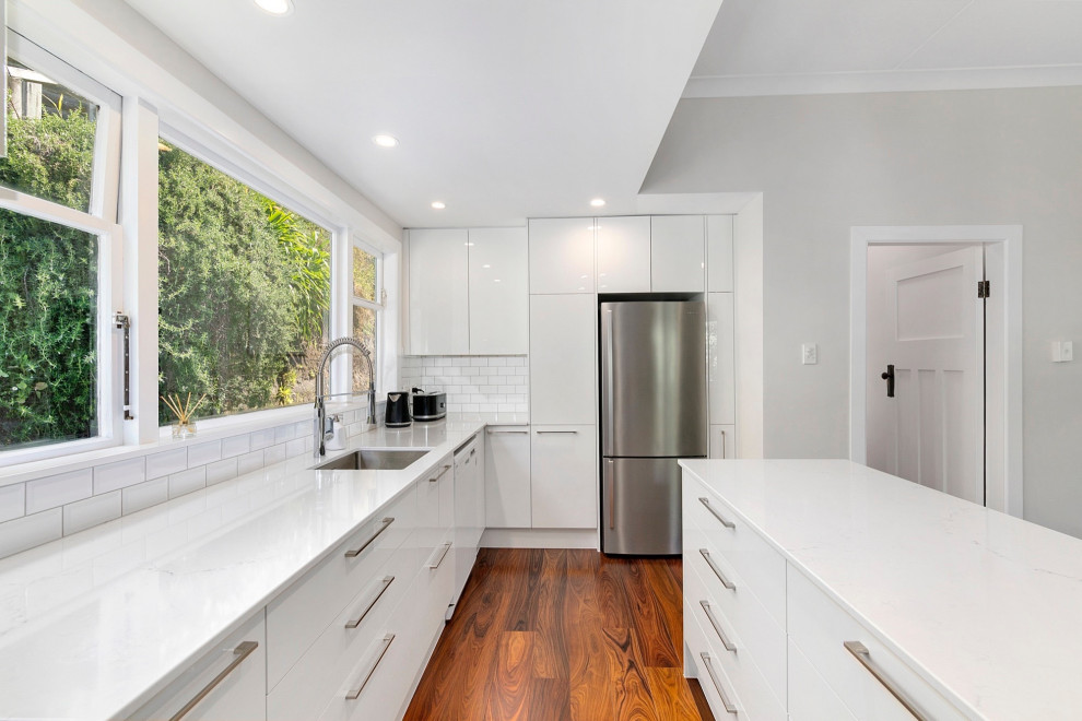 This is an example of a large contemporary galley eat-in kitchen in Sydney with recessed-panel cabinets, white cabinets, granite benchtops, white splashback, porcelain splashback, stainless steel appliances, dark hardwood floors, with island and white benchtop.