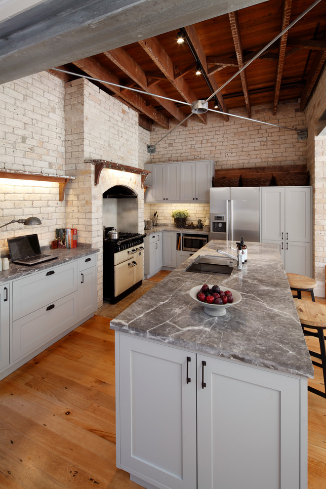 Industrial l-shaped eat-in kitchen in Sydney with an undermount sink, grey cabinets, marble benchtops, beige splashback, stainless steel appliances, black walls, medium hardwood floors and with island.