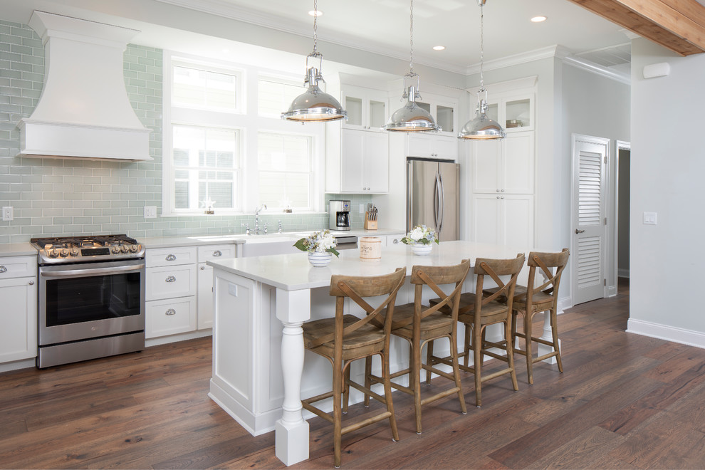 This is an example of a mid-sized beach style kitchen in New York with a farmhouse sink, shaker cabinets, white cabinets, quartzite benchtops, green splashback, glass tile splashback, stainless steel appliances, medium hardwood floors, with island and white benchtop.