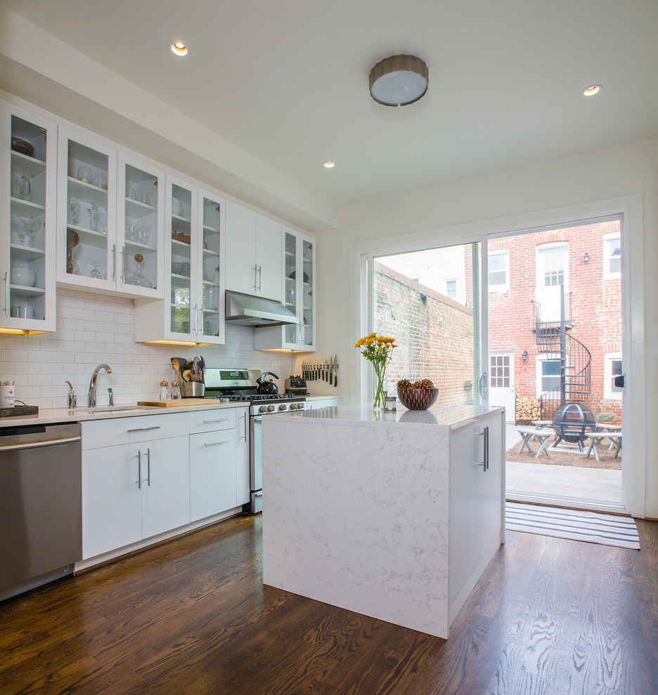 Inspiration for a contemporary kitchen in DC Metro with flat-panel cabinets, white cabinets, quartz benchtops, white splashback, ceramic splashback, stainless steel appliances, medium hardwood floors and with island.