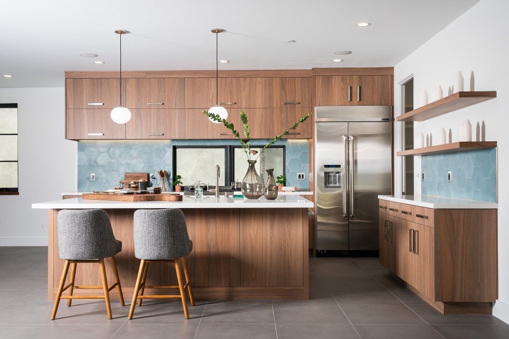 Contemporary l-shaped kitchen in Los Angeles with flat-panel cabinets, medium wood cabinets, blue splashback, stainless steel appliances, with island, grey floor and white benchtop.