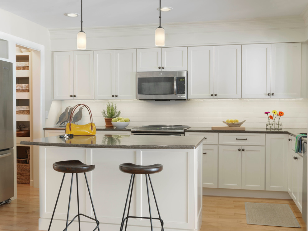 Inspiration for a transitional l-shaped kitchen in Burlington with shaker cabinets, white cabinets, white splashback, ceramic splashback, stainless steel appliances, light hardwood floors and with island.