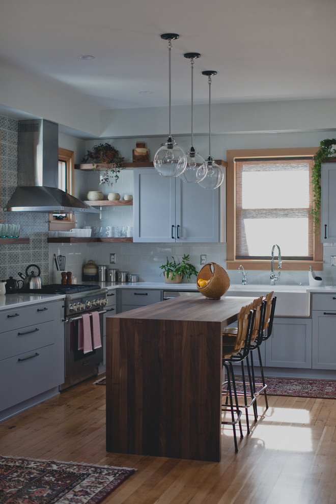 Mid-sized transitional l-shaped light wood floor eat-in kitchen photo in Portland with a farmhouse sink, shaker cabinets, gray cabinets, quartz countertops, blue backsplash, ceramic backsplash, stainless steel appliances and an island