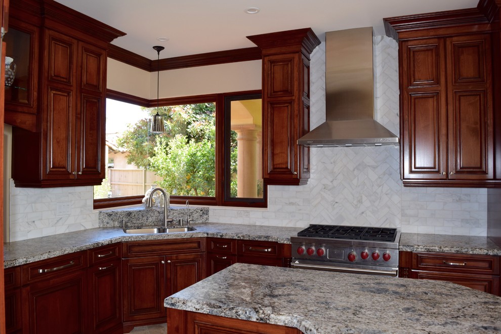 Mid-sized traditional u-shaped eat-in kitchen in San Diego with a double-bowl sink, raised-panel cabinets, red cabinets, granite benchtops, grey splashback, stone tile splashback, stainless steel appliances, travertine floors and with island.
