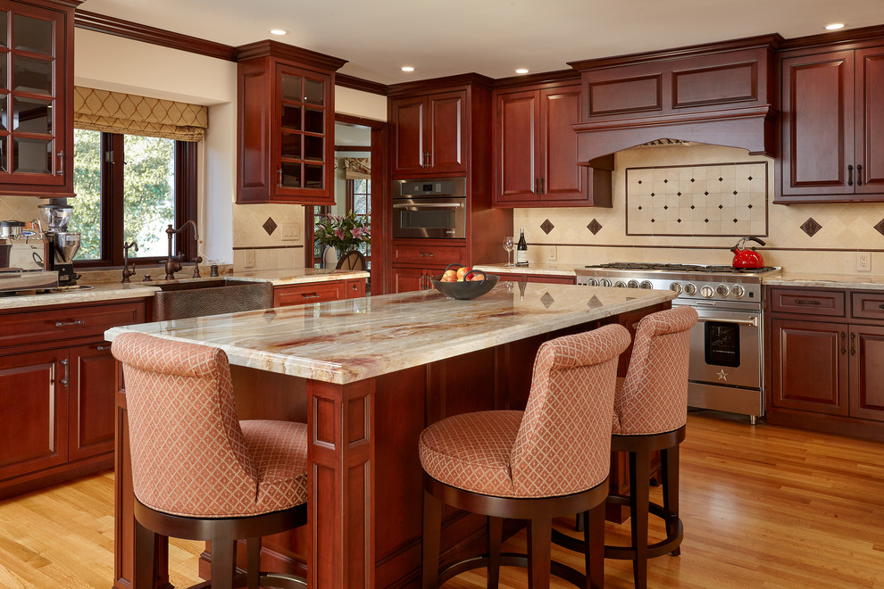 Large elegant l-shaped medium tone wood floor and brown floor open concept kitchen photo in San Francisco with a farmhouse sink, dark wood cabinets, granite countertops, beige backsplash, limestone backsplash, stainless steel appliances, raised-panel cabinets, an island and beige countertops