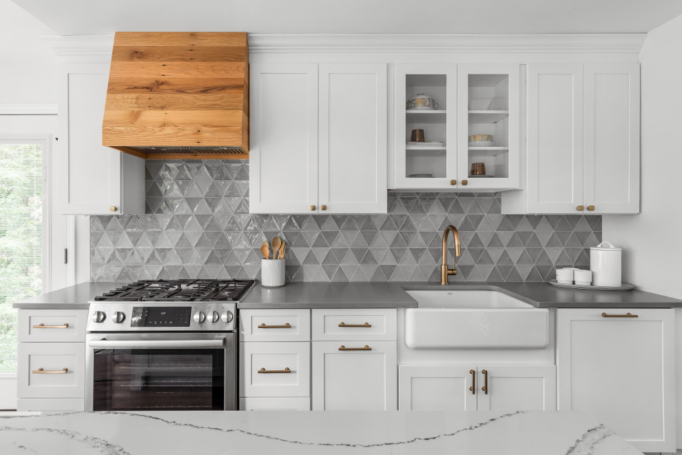 Mid-sized transitional l-shaped dark wood floor and brown floor open concept kitchen photo in New York with a farmhouse sink, shaker cabinets, white cabinets, quartz countertops, gray backsplash, glass tile backsplash, stainless steel appliances, an island and gray countertops