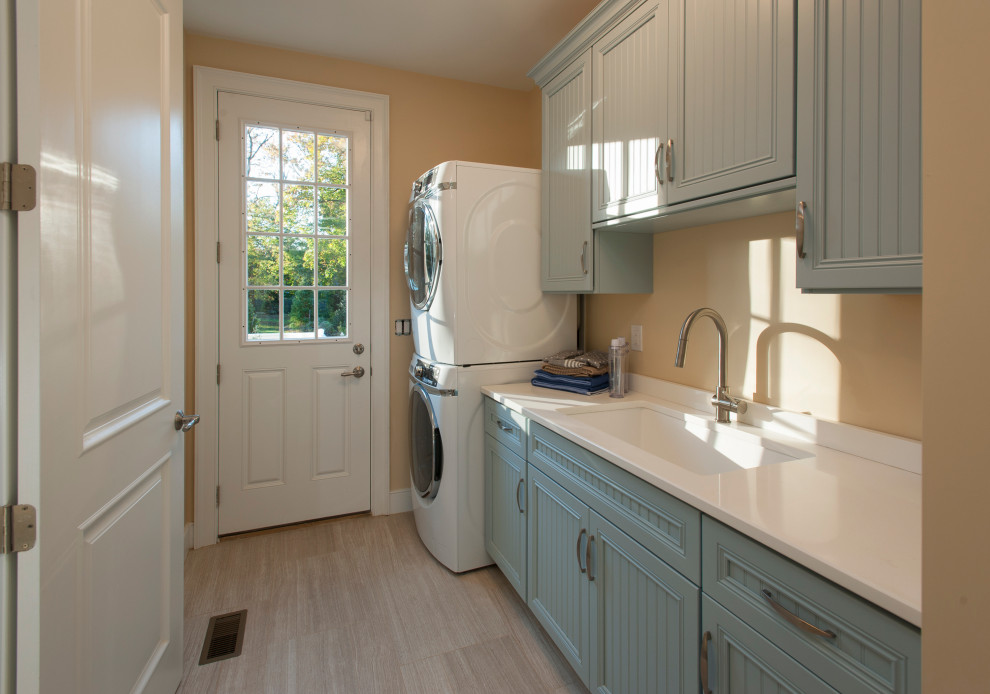 Inspiration for a mid-sized transitional galley dedicated laundry room in Philadelphia with an undermount sink, turquoise cabinets, beige walls and a stacked washer and dryer.