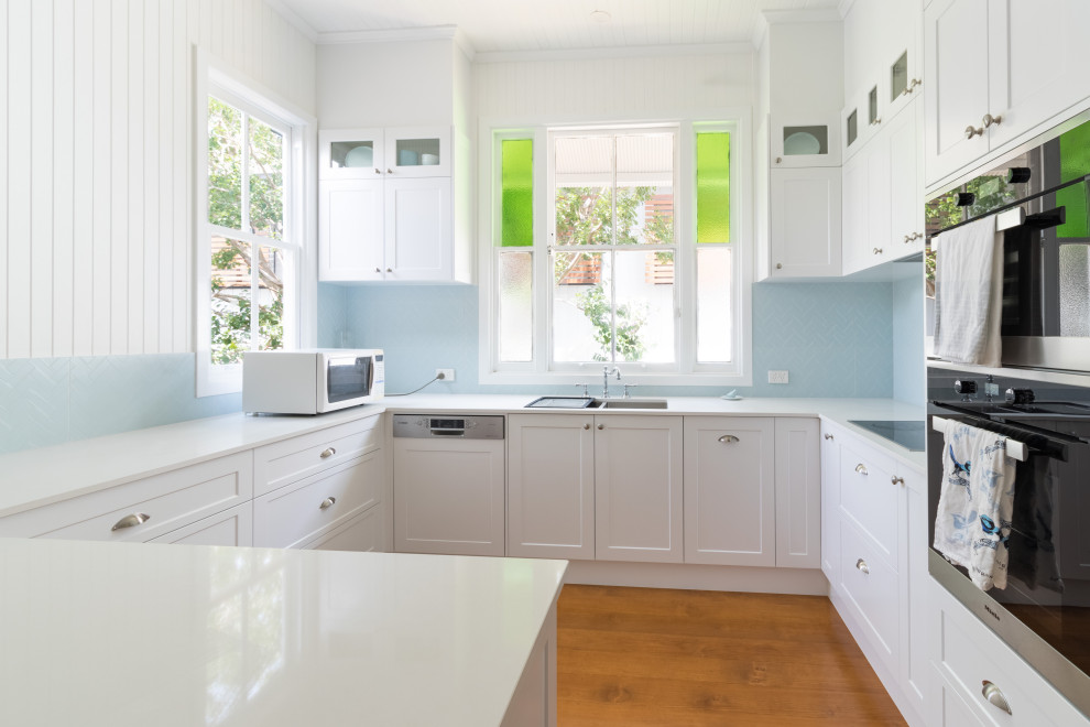 This is an example of a mid-sized traditional u-shaped separate kitchen in Brisbane with a drop-in sink, white cabinets, blue splashback, ceramic splashback, white appliances, light hardwood floors, no island, white benchtop, timber, recessed-panel cabinets and quartz benchtops.