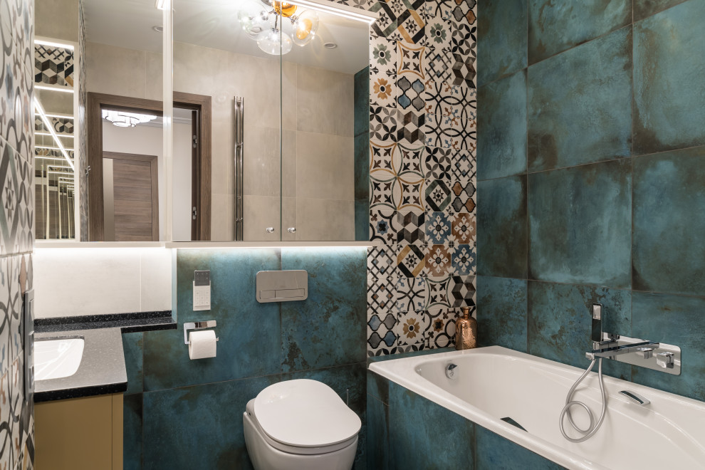 Mid-sized contemporary bathroom in Saint Petersburg with flat-panel cabinets, yellow cabinets, an undermount tub, a shower/bathtub combo, a wall-mount toilet, multi-coloured tile, porcelain floors, solid surface benchtops, turquoise floor, an open shower and black benchtops.