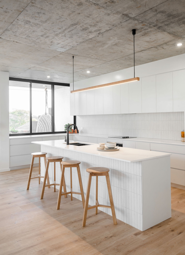 Design ideas for a large contemporary l-shaped kitchen in Sydney with an undermount sink, flat-panel cabinets, white cabinets, white splashback, porcelain splashback, panelled appliances, with island, beige floor and white benchtop.