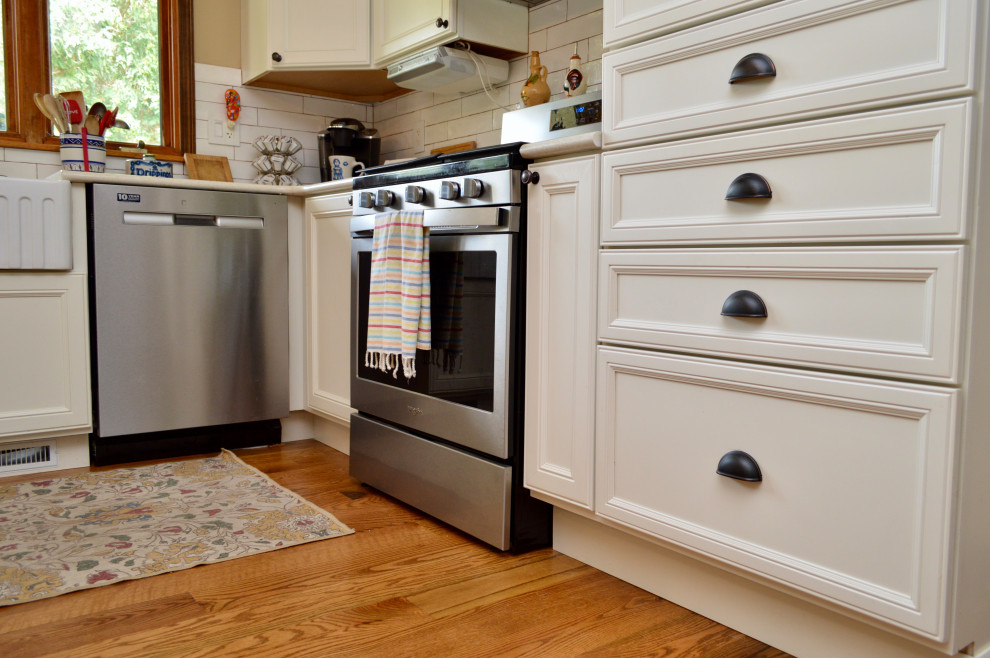 Klassisk inredning av ett mellanstort vit vitt kök, med en undermonterad diskho, luckor med infälld panel, vita skåp, bänkskiva i kvartsit, vitt stänkskydd, stänkskydd i keramik, rostfria vitvaror, mellanmörkt trägolv, en halv köksö och brunt golv