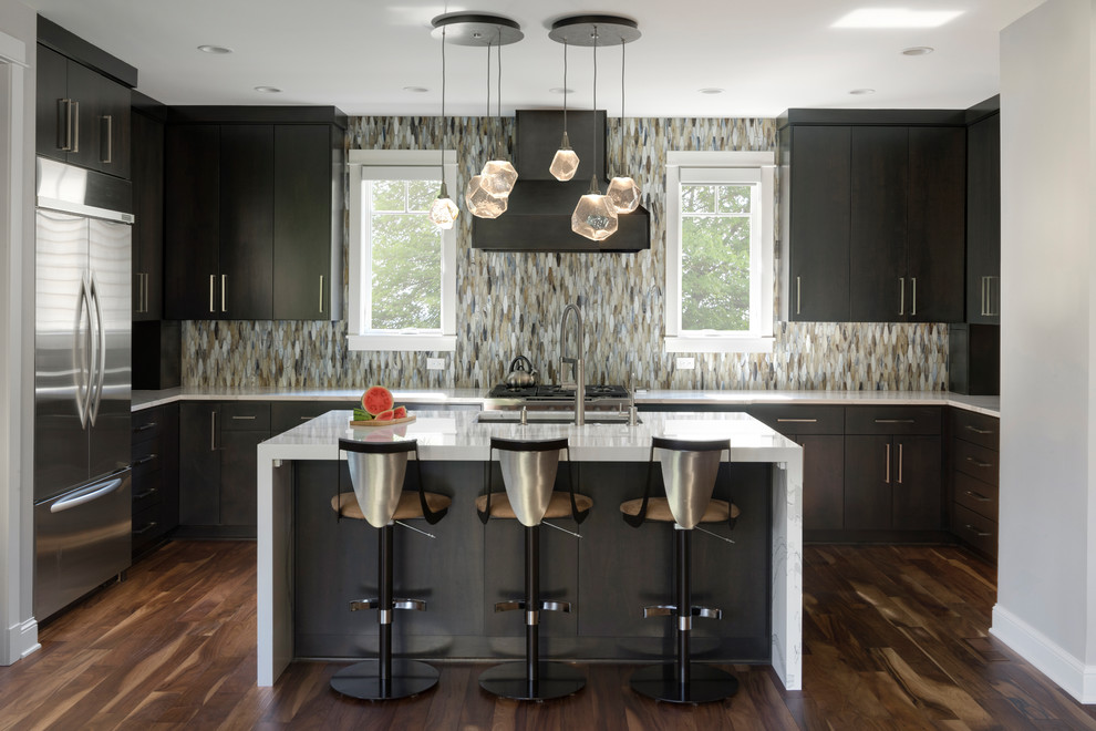 This is an example of a contemporary u-shaped kitchen in Minneapolis with an undermount sink, flat-panel cabinets, dark wood cabinets, multi-coloured splashback, mosaic tile splashback, stainless steel appliances, dark hardwood floors, with island, brown floor and white benchtop.