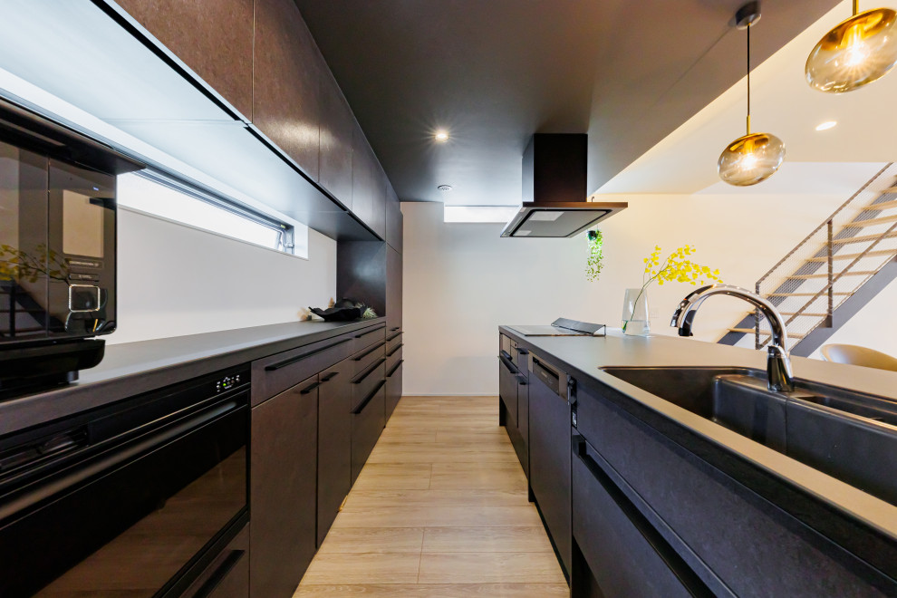 Стильный дизайн: прямая кухня-гостиная среднего размера в стиле модернизм с черными фасадами, черным фартуком, паркетным полом среднего тона, коричневым полом, черной столешницей, потолком с обоями и мойкой у окна - последний тренд