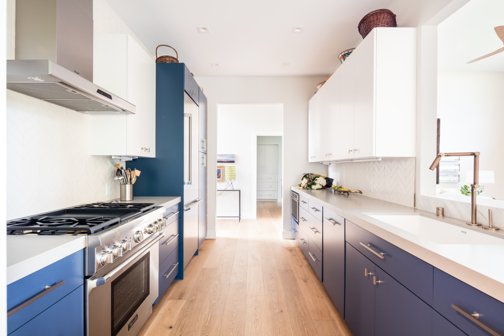 Inspiration for a mid-sized contemporary galley medium tone wood floor and brown floor kitchen remodel in Orange County with flat-panel cabinets, no island, an undermount sink, blue cabinets, white backsplash, stainless steel appliances and gray countertops