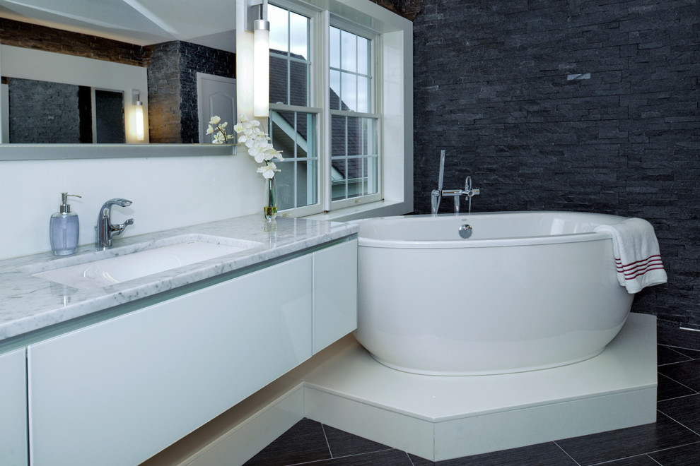 This is an example of a large contemporary master bathroom in Other with flat-panel cabinets, white cabinets, a freestanding tub, gray tile, stone tile, grey walls, porcelain floors, an undermount sink, marble benchtops and grey floor.
