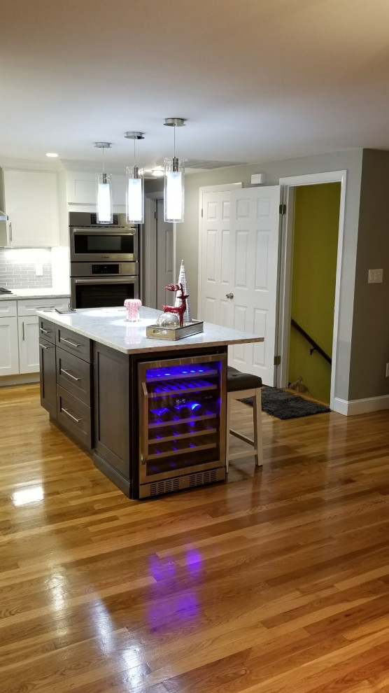 Inspiration for a mid-sized transitional l-shaped dark wood floor and brown floor open concept kitchen remodel with an undermount sink, shaker cabinets, white cabinets, gray backsplash, stainless steel appliances, an island and white countertops