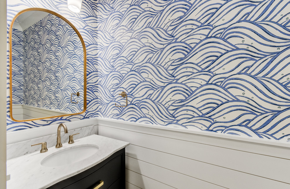 Bild på ett litet maritimt grå grått toalett, med luckor med profilerade fronter, blå skåp, blå väggar, mellanmörkt trägolv, ett undermonterad handfat, marmorbänkskiva och brunt golv
