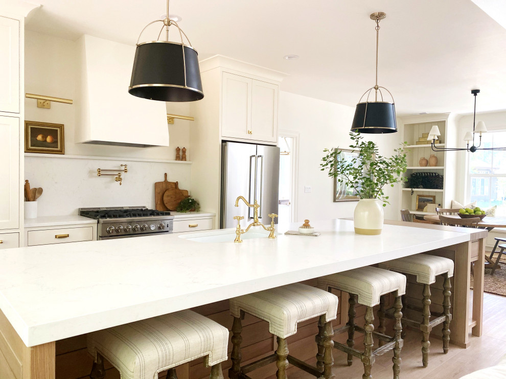 Transitional l-shaped light wood floor and beige floor kitchen photo in Seattle with an undermount sink, shaker cabinets, white cabinets, white backsplash, stainless steel appliances, an island and white countertops