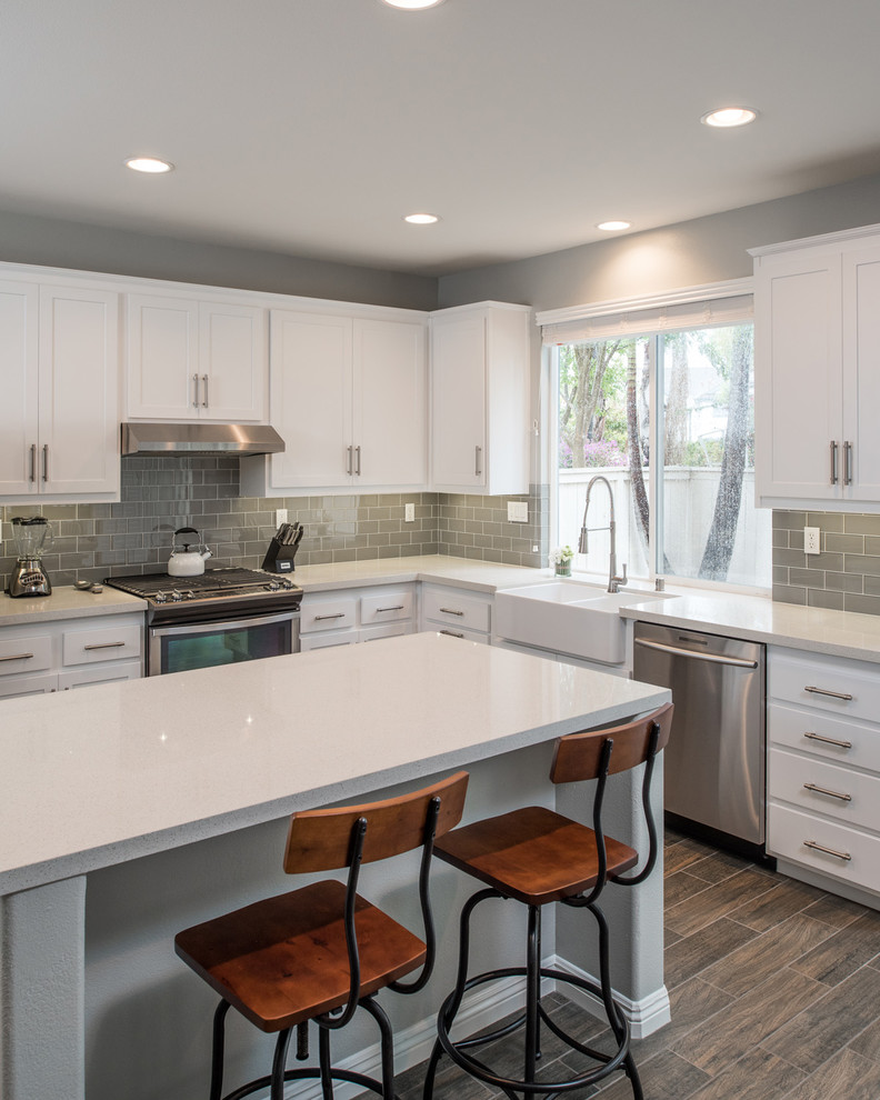 Design ideas for a mid-sized modern u-shaped kitchen in San Diego with a farmhouse sink, shaker cabinets, white cabinets, quartz benchtops, grey splashback, subway tile splashback, stainless steel appliances, plywood floors and with island.
