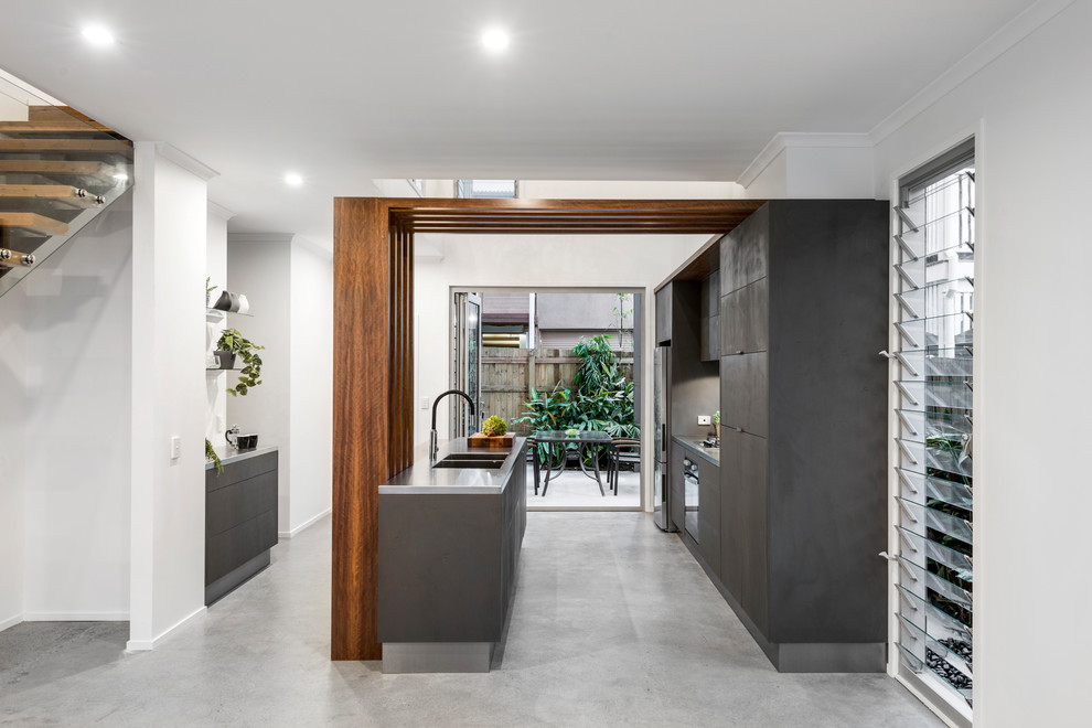 This is an example of a small modern galley open plan kitchen in Brisbane with flat-panel cabinets, grey cabinets, stainless steel benchtops, glass sheet splashback, stainless steel appliances, concrete floors, with island and grey floor.