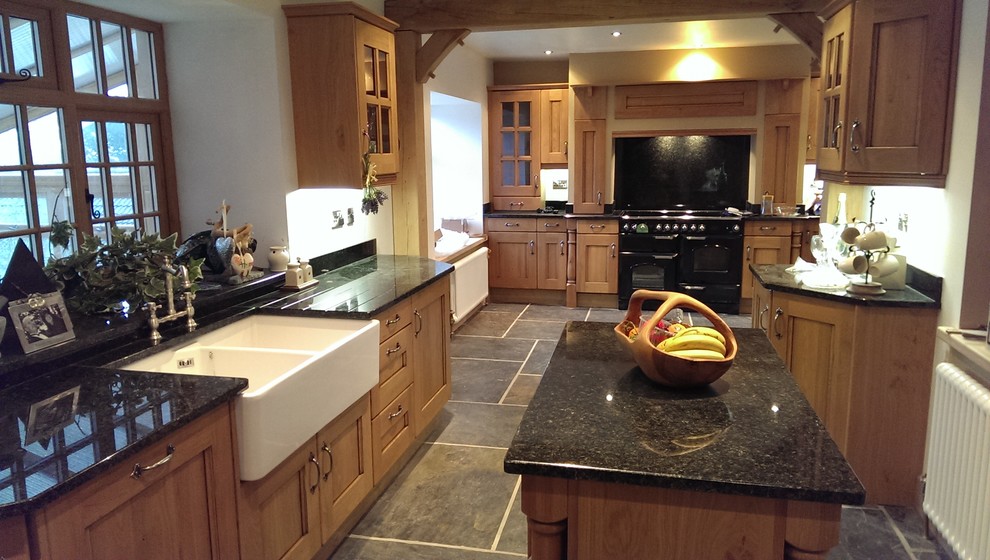 This is an example of a large country u-shaped separate kitchen in Other with with island, beaded inset cabinets, medium wood cabinets, granite benchtops, black splashback, stone slab splashback, black appliances, a double-bowl sink and porcelain floors.