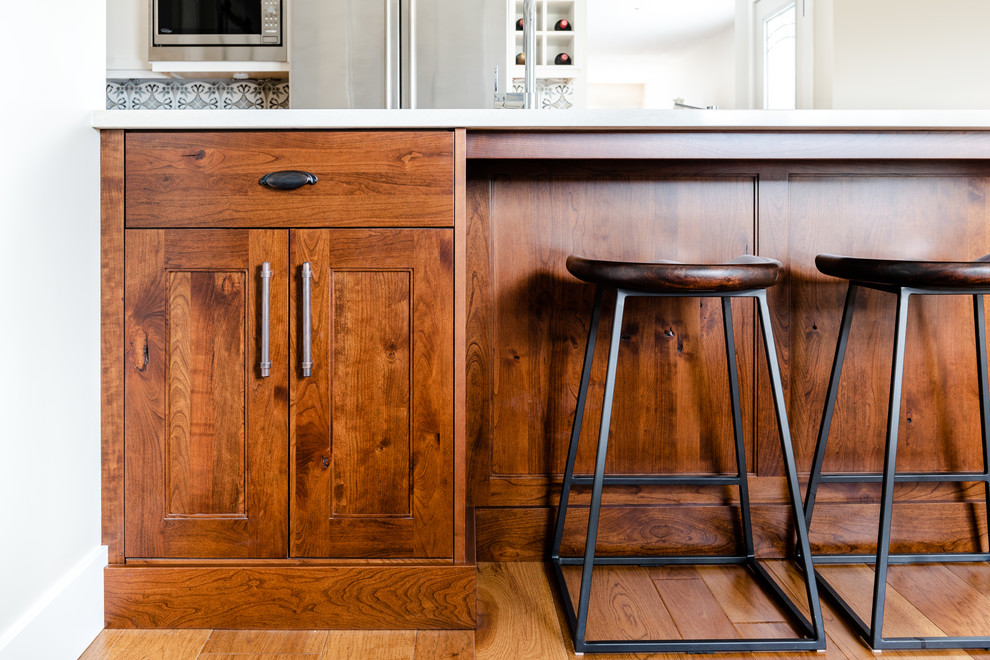 Inspiration for a mid-sized transitional l-shaped medium tone wood floor and brown floor kitchen pantry remodel with an undermount sink, shaker cabinets, white cabinets, quartzite countertops, gray backsplash, porcelain backsplash, stainless steel appliances, an island and white countertops