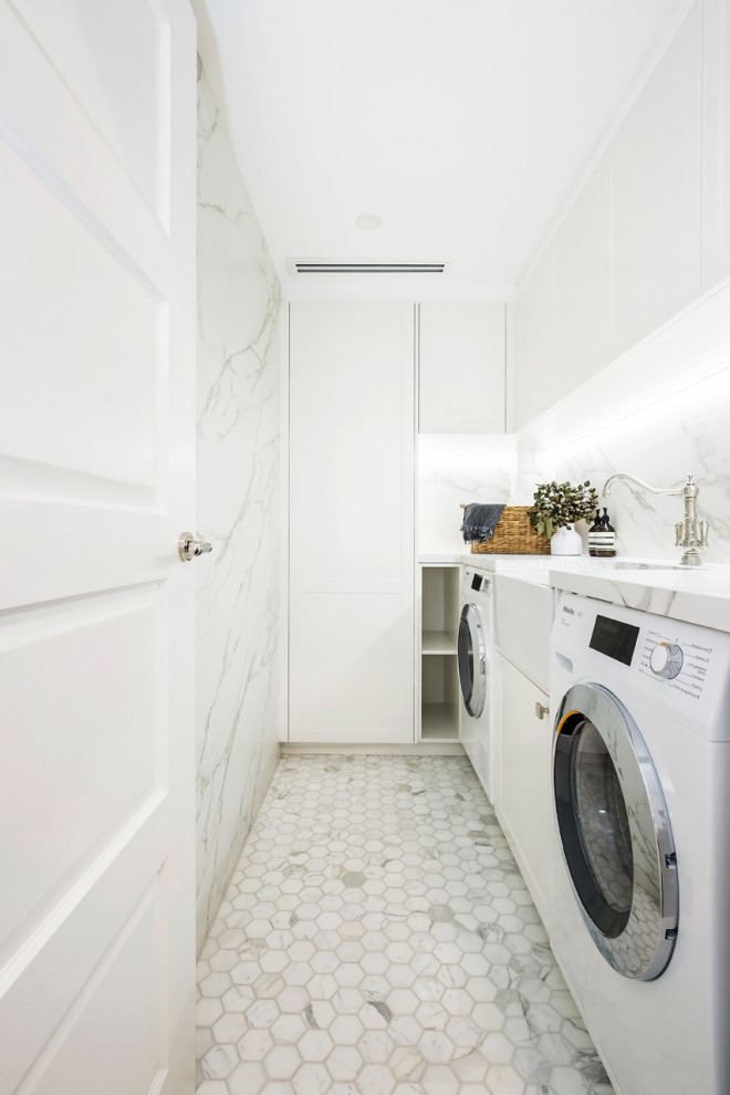 This is an example of a mid-sized transitional l-shaped dedicated laundry room in Sydney with a farmhouse sink, recessed-panel cabinets, white cabinets, marble benchtops, multi-coloured splashback, marble splashback, white walls, medium hardwood floors, an integrated washer and dryer, white floor and multi-coloured benchtop.