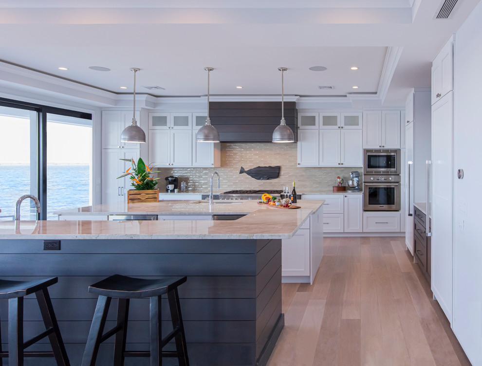 Kitchen - coastal l-shaped light wood floor and beige floor kitchen idea in New York with an undermount sink, shaker cabinets, white cabinets, beige backsplash, stainless steel appliances, two islands and beige countertops