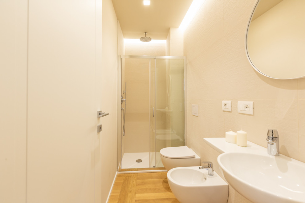 Eklektisk inredning av ett mellanstort badrum med dusch, med en kantlös dusch, en vägghängd toalettstol, vit kakel, vita väggar, ljust trägolv, ett fristående handfat, kaklad bänkskiva och dusch med skjutdörr