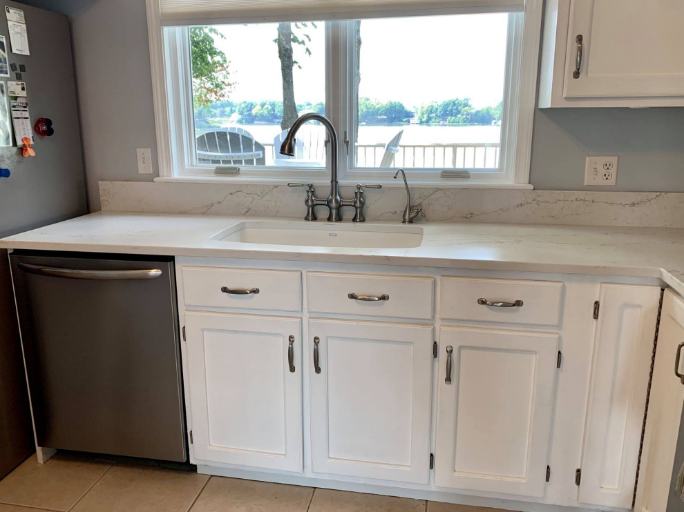 This is an example of a small beach style l-shaped eat-in kitchen in Indianapolis with an undermount sink, recessed-panel cabinets, white cabinets, quartz benchtops, ceramic floors, no island, brown floor and white benchtop.