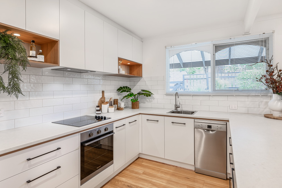 Design ideas for a mid-sized contemporary u-shaped eat-in kitchen in Adelaide with a single-bowl sink, white cabinets, laminate benchtops, white splashback, subway tile splashback, stainless steel appliances, medium hardwood floors, a peninsula, brown floor and white benchtop.