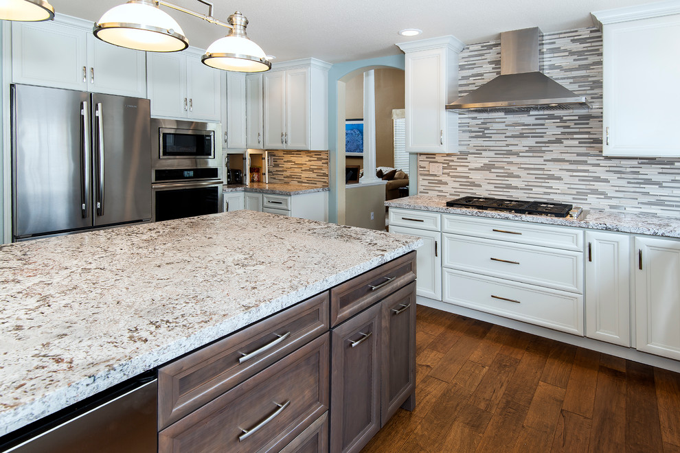 Large transitional medium tone wood floor enclosed kitchen photo with a farmhouse sink, recessed-panel cabinets, white cabinets, granite countertops, multicolored backsplash, matchstick tile backsplash, stainless steel appliances and an island