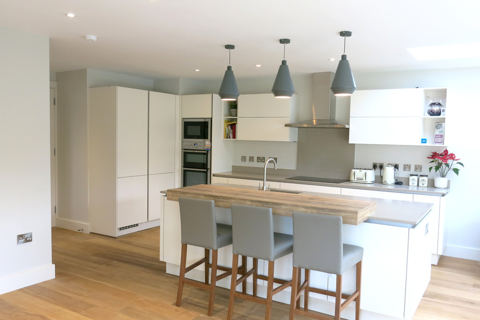 Design ideas for a large contemporary l-shaped eat-in kitchen in Dublin with an undermount sink, flat-panel cabinets, white cabinets, wood benchtops, grey splashback, stainless steel appliances, a peninsula and light hardwood floors.