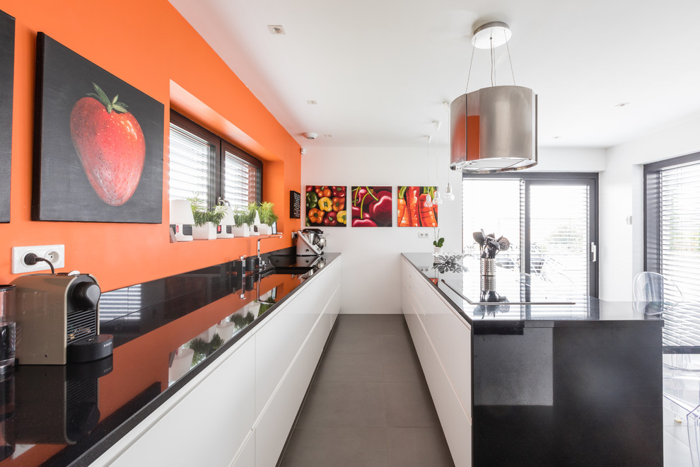 Photo of a mid-sized contemporary galley open plan kitchen in Strasbourg with an undermount sink, white cabinets, granite benchtops, orange splashback, black appliances, ceramic floors, grey floor, flat-panel cabinets and a peninsula.