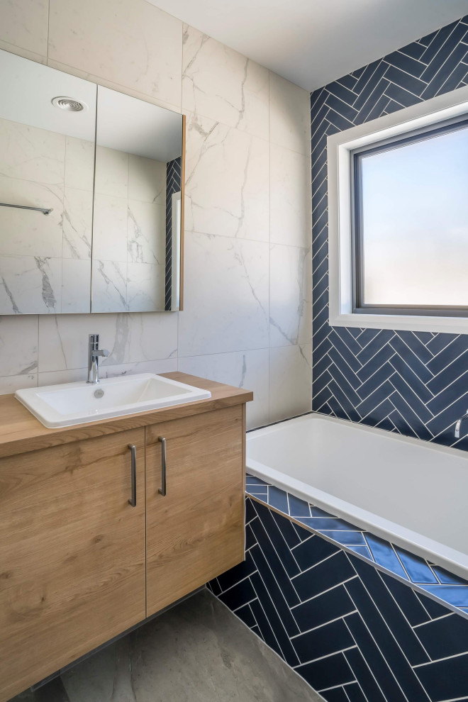 Exemple d'une salle de bain tendance en bois clair de taille moyenne avec un placard à porte plane, un carrelage bleu, un carrelage métro, un sol en carrelage de céramique, un plan de toilette en stratifié, un sol gris, un plan de toilette marron, meuble simple vasque et meuble-lavabo suspendu.