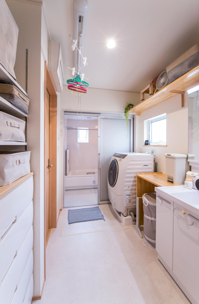Design ideas for a scandinavian single-wall laundry room in Other with a single-bowl sink, flat-panel cabinets, white cabinets, solid surface benchtops, white walls, vinyl floors, a side-by-side washer and dryer and white floor.
