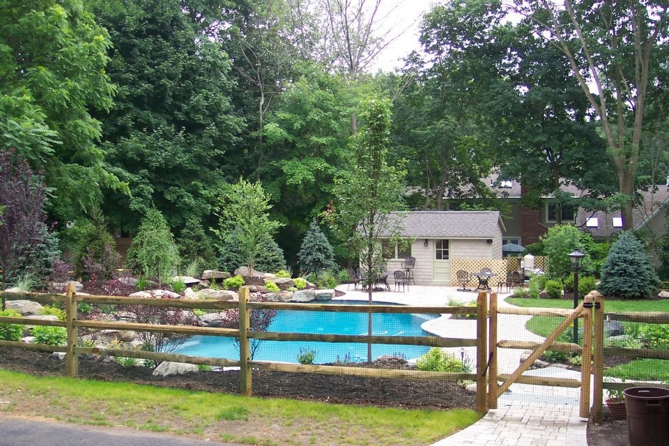 Large country backyard custom-shaped natural pool in New York with brick pavers.